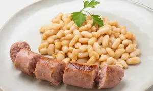 Un plato de alubias blancas tiernas y jugosas salchichas, decorado con una ramita de perejil fresco.