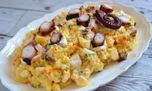 Deliciosa ensaladilla de pulpo con patatas, huevo y zanahoria, coronada con trozos de pulpo tierno y un toque de mayonesa.