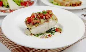 Filete de bacalao con tomate y hierbas, sobre espinacas y salsa cremosa. Un plato principal ideal para tus recetas de bacalao.