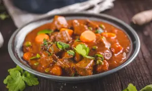 Un plato humeante de rabo de ternera estofado con zanahorias y guisantes, adornado con perejil fresco.