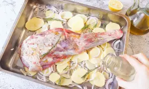 Paletilla de cordero al horno lista para asar con patatas, cebolla y romero. Un chorrito de aceite y al horno.