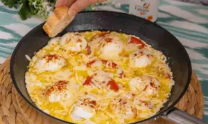 Huevos turcos recién hechos en sartén, con tomate y queso fundido, listos para mojar pan.