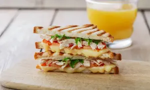 Delicioso sandwich de pollo a la parrilla con queso derretido, tomate y lechuga, acompañado de un vaso de jugo de naranja.