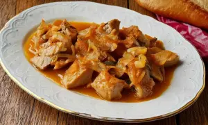 Sabroso atún encebollado en una salsa dorada, servido en un plato blanco con borde dorado.