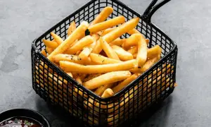 Patatas soufflé doradas y crujientes en una cesta negra, listas para ser disfrutadas con una salsa.