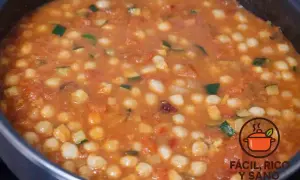 Un guiso casero de garbanzos con verduras, como calabacín y tomate, burbujeando en una olla.