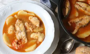 Un plato humeante de suquet de pescado, con trozos de pescado blanco, patatas y gambas en una rica salsa.