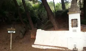En la ruta de las fuentes, un cartel indica "AIGUA NO POTABLE" junto a una fuente de piedra y un pequeño altar en un bosque.
