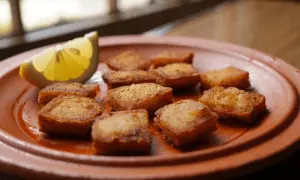 Deliciosos trozos de bacalao rebozado, dorados y crujientes, servidos en un plato de barro con una rodaja de limón.