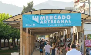 Gente pasea por un mercadillo en Benicàssim, bajo un cartel azul que anuncia "Mercado Artesanal Torre de Sant Vicent".