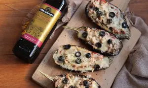 Berenjenas rellenas gratinadas con queso y aceitunas, junto a una botella de aceite de oliva virgen extra Oleoestepa.