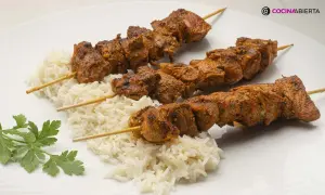 Tres pinchos morunos jugosos sobre una cama de arroz blanco, decorados con perejil fresco.