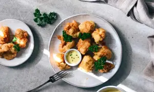 Crujiente coliflor rebozada, dorada y servida con salsa de mostaza y perejil fresco. ¡Un aperitivo delicioso!