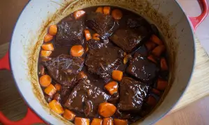 Boeuf bourguignon cocinado a fuego lento en una olla roja, con trozos de carne tierna, zanahorias y champiñones en una rica salsa.