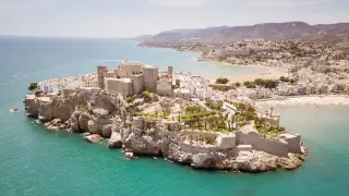 Castillo medieval en un acantilado rocoso sobre el mar turquesa, con un pueblo blanco y playas doradas. Un rincón idílico de la costa del azahar.