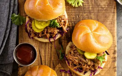 Dos jugosos sándwiches de pulled pork con pepinillos y col morada sobre pan rústico, listos para disfrutar.