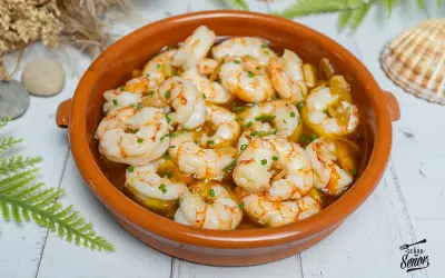 Un plato de gambas al ajillo burbujeantes en una cazuela de barro, adornado con perejil picado.