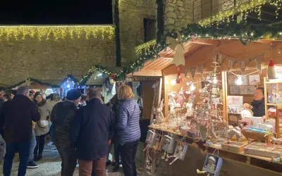 Gente pasea por el mercado navideño Peñíscola, con puestos de adornos y luces festivas.