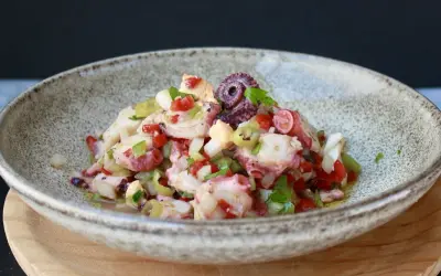 Salpicon de pulpo fresco con pimientos, cebolla y perejil, servido en un cuenco rústico.