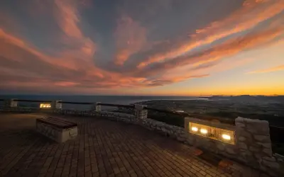 Atardecer espectacular sobre el mar y la costa. Un mirador perfecto para ver qué ver en Alcossebre, con un banco y luces que invitan a contemplar.