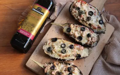 Berenjenas rellenas gratinadas con queso y aceitunas, junto a una botella de aceite de oliva virgen extra Oleoestepa.