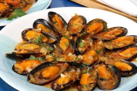 Un plato de mejillones a la marinera, jugosos y con una salsa sabrosa, adornados con perejil fresco.