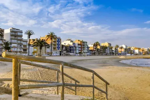 Escaleras de madera bajan a una playa vacía con edificios coloridos y palmeras al fondo. Un ejemplo de pueblos bonitos cerca de Benicàssim.