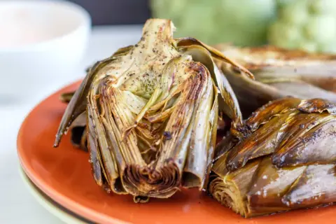 Deliciosas alcachofas al horno, doradas y tiernas, servidas en un plato naranja. Perfectas para disfrutar de su sabor.