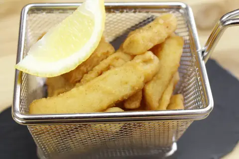 Deliciosos chocos fritos crujientes en una cesta metálica, acompañados de una rodaja de limón.