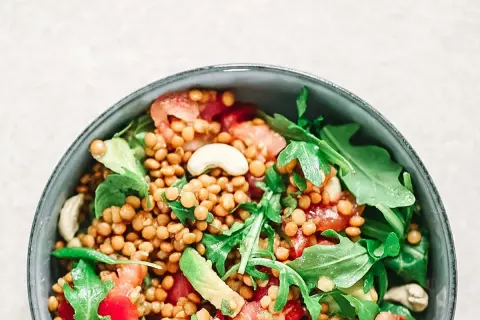 Deliciosa ensalada de lentejas con aguacate, tomate y rúcula, coronada con anacardos. Un plato fresco y nutritivo.