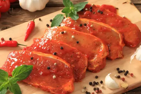 Filetes de lomo adobado listos para cocinar, con pimientos rojos, ajo y hierbas frescas.