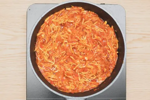 Tinga de pollo cocinándose en una sartén, con trozos de pollo deshebrado y salsa roja.
