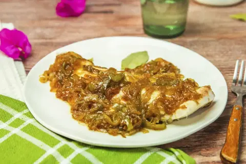 Un plato de urta a la roteña, con su jugoso pescado cubierto de cebolla y pimientos caramelizados, listo para disfrutar.