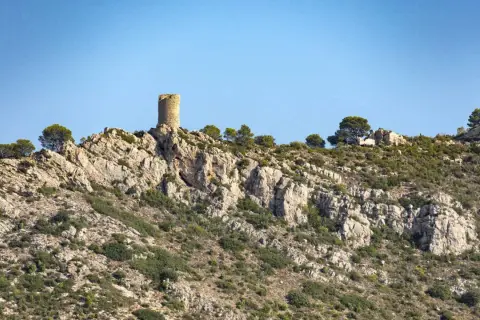Torreón solitario en la cima rocosa del Desierto de las Palmas, vigilando un paisaje árido y escarpado bajo un cielo azul.
