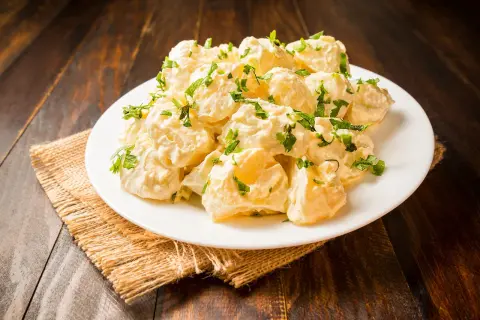 Patatas alioli cremosas y deliciosas, cubiertas con perejil fresco, servidas en un plato blanco sobre una mesa de madera rústica.