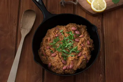 Un delicioso chili con carne humeante en sartén de hierro fundido, adornado con frijoles rojos y cilantro fresco.