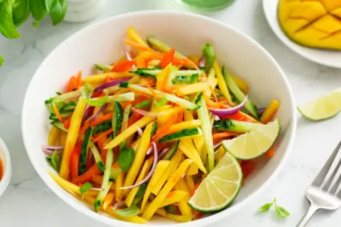 Ensalada de mango vibrante con pepino, zanahoria, cebolla morada y pimientos, aderezada con lima.
