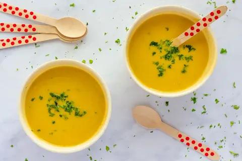 Dos cuencos de cremoso pure de verduras, decorados con perejil picado y cucharas de madera con lunares rojos.