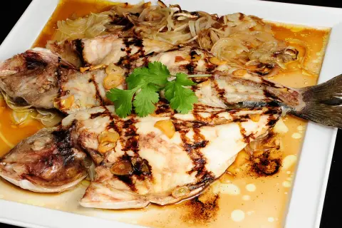 Dorada a la espalda, jugosa y a la parrilla, servida con cebolla caramelizada, ajo y cilantro fresco en una salsa dorada.