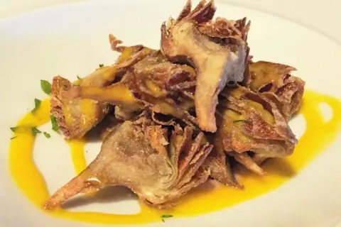 Deliciosas alcachofas fritas crujientes, servidas con una salsa dorada y perejil picado.