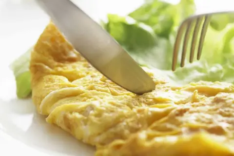 Un cuchillo corta una dorada tortilla francesa junto a hojas de lechuga fresca.