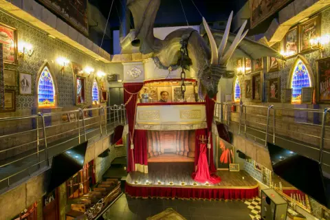 Dragón suspendido sobre un escenario teatral en el magic museum Peñíscola. Ventanas góticas y pósters de ilusionismo adornan las paredes.