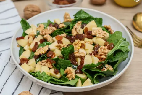 Deliciosa ensalada de espinacas con trozos de manzana, pasas y nueces crujientes. Un festín de texturas y sabores.