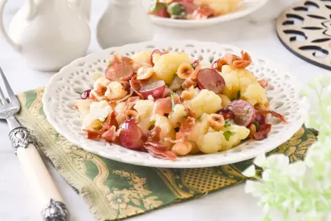 Deliciosa ensalada de coliflor con uvas rojas, prosciutto crujiente y avellanas tostadas. Un plato fresco y lleno de sabor.