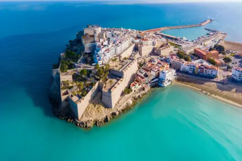 Castellón Costa Azahar: un pueblo amurallado con un castillo se alza sobre el mar turquesa, con un puerto deportivo y playas doradas.