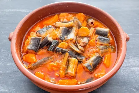Un cuenco de barro con un delicioso all i pebre, un guiso tradicional de anguilas y patatas en salsa roja.