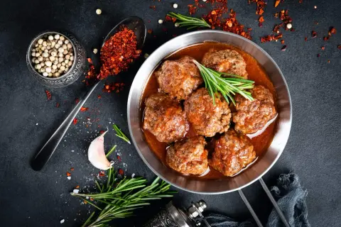 Sabrosas albóndigas con tomate, servidas en sartén, con romero, ajo y especias.