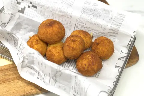Croquetas de gambas doradas y crujientes, servidas en una bandeja con papel de periódico.