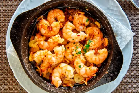 Deliciosos langostinos al ajillo burbujeando en aceite de oliva, con trozos de ajo y perejil fresco. ¡Un plato que huele a gloria!