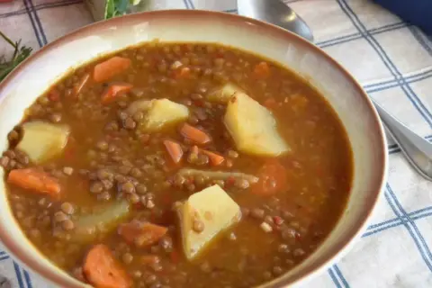 Un tazón humeante de lentejas estofadas Arguiñano, con patatas y zanahorias, listo para disfrutar.